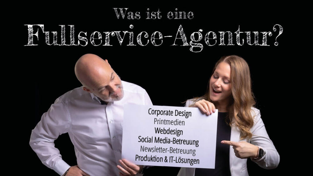 Was ist eine Fullservice-Agentur? Johannes und Sabrina mit weißen Schild in der Hand auf dem steht: Coporate Design, Printmedien, Webdesign, Social Media Betreuung, Newsletter Betreuung, Produktion und IT Lösungen